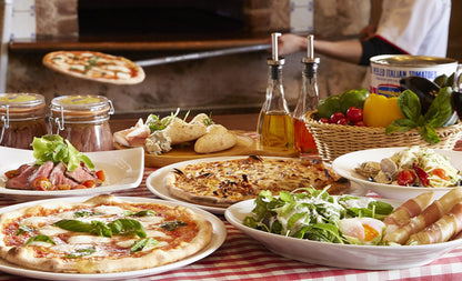 Table with various pizzas, salads, and side dishes in a casual dining setting.